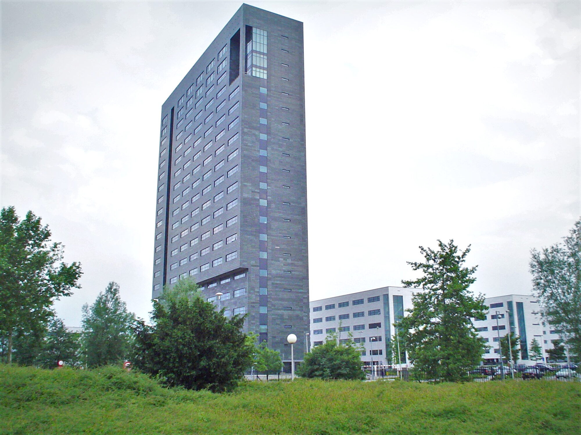 A tall dark-clad office tower on ASML's Veldhoven campus in the Netherlands, with lower white buildings beside it