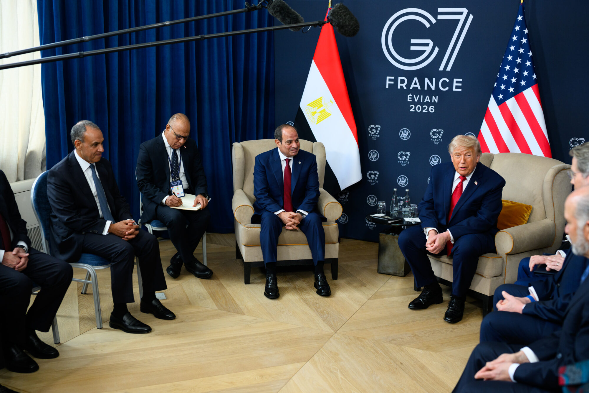 Egyptian President Abdel Fattah el-Sisi seated in an armchair beside Egyptian and US flags during a bilateral meeting at the 2026 G7 in Evian