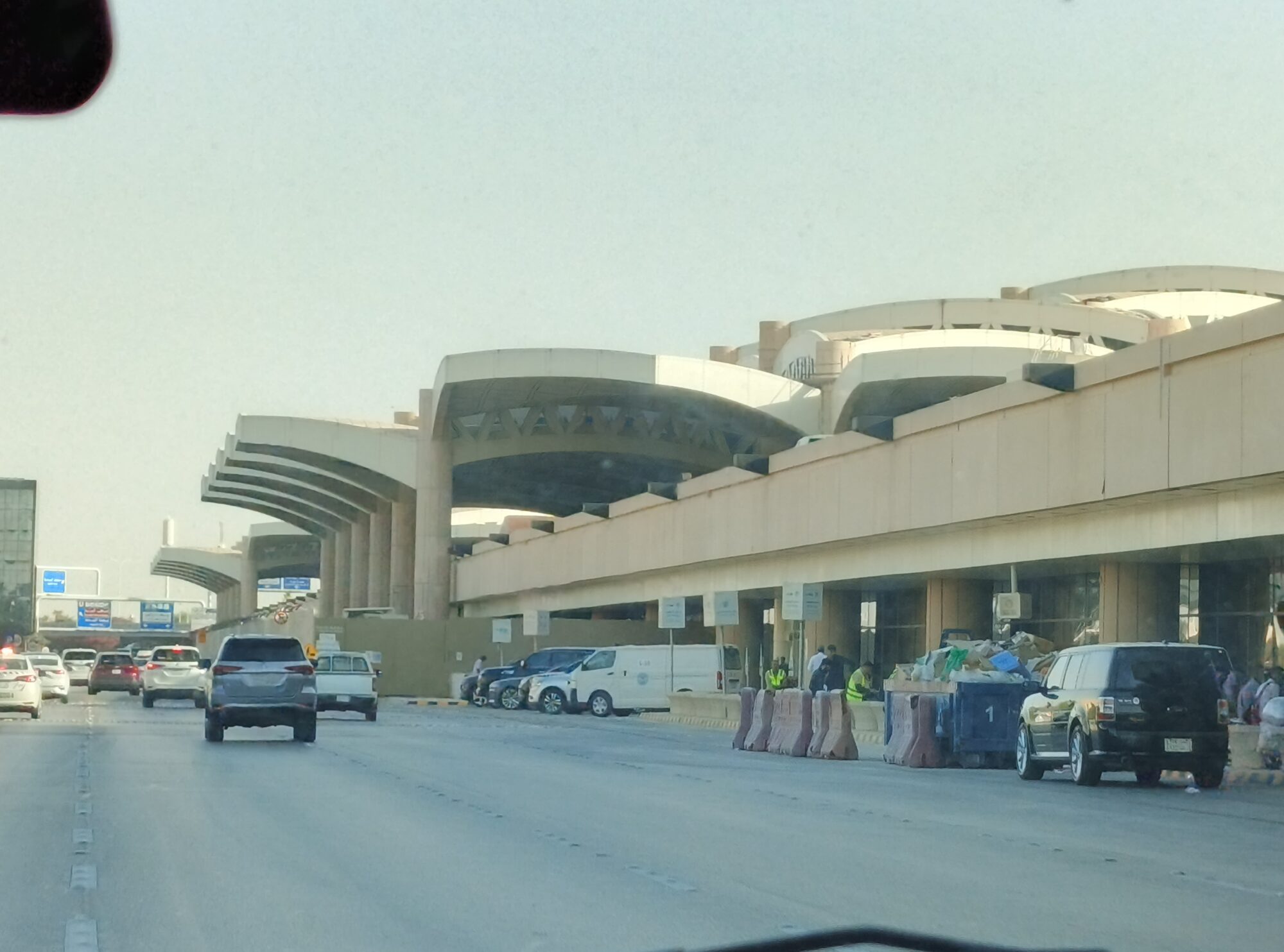 Curved concrete canopies of a passenger terminal at King Khalid International Airport in Riyadh, with cars on the access road