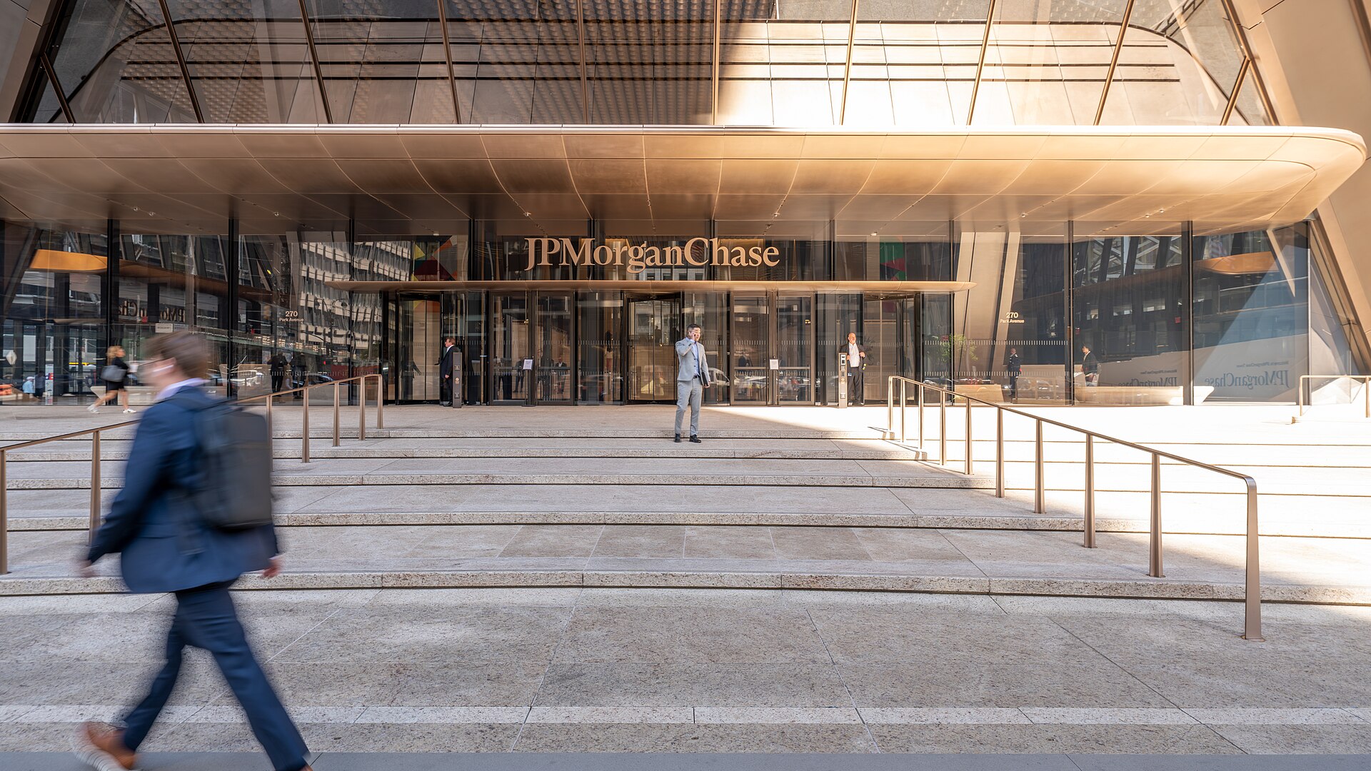 The entrance of JPMorgan Chase's 270 Park Avenue headquarters in New York, with the bank's name above the doors and a commuter walking past
