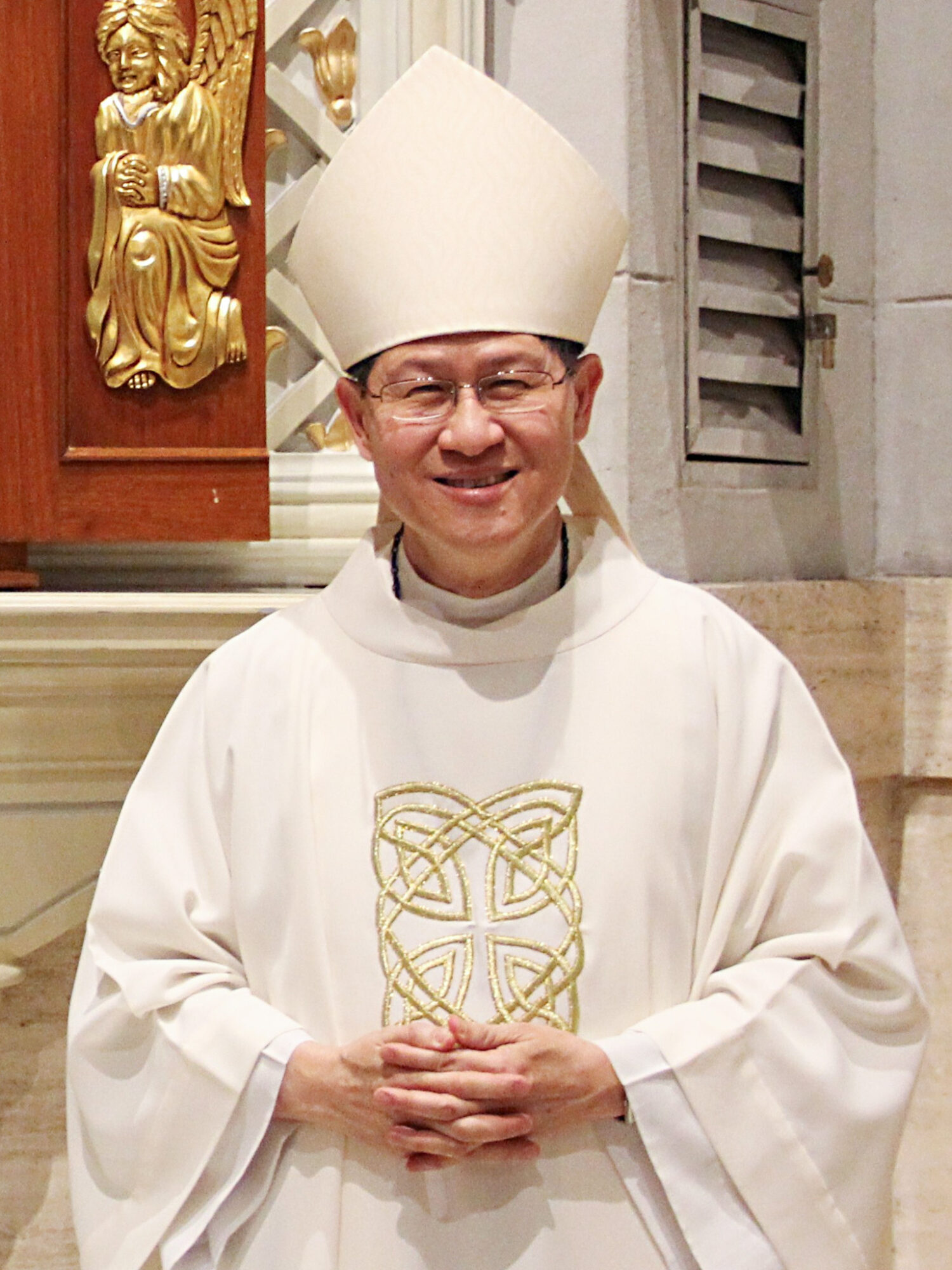 Smiling Cardinal Luis Antonio Tagle in cream vestments and mitre inside a church